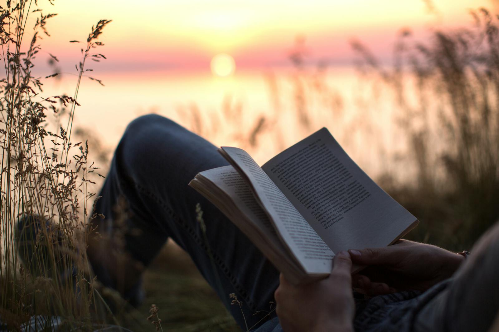 Person enjoys a peaceful moment reading by the sea at sunset, surrounded by nature.